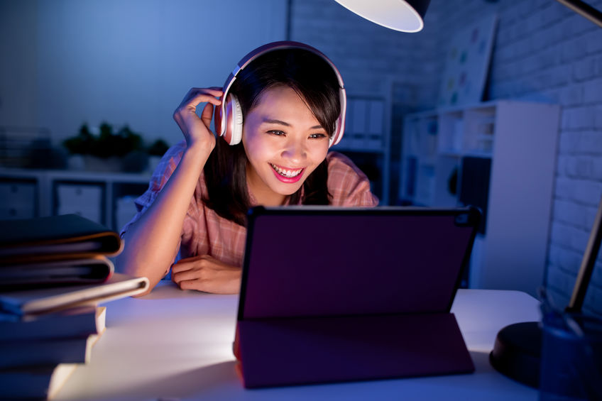 Asian woman with pink headphones smiling at her digital tablet screen