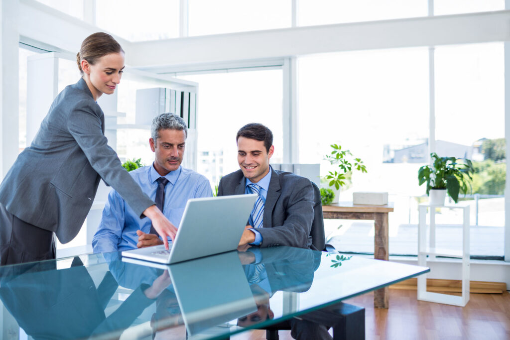 Three business people surrounding a laptop on a desk in a well-lit office