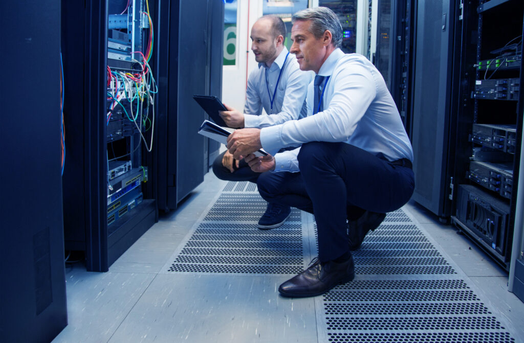 Two male IT professionals crouching in a server room looking at cords